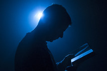 Man holding Bible with light from behind and blue tones