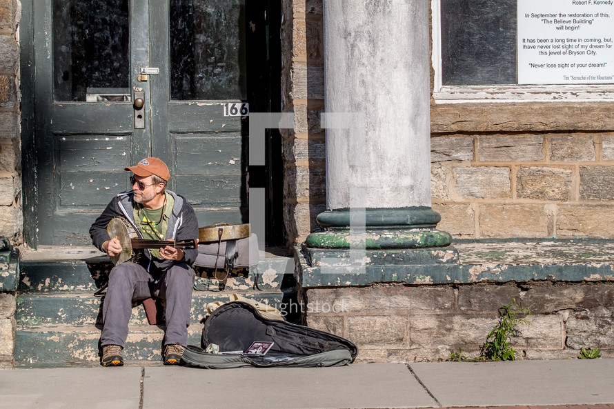 Man playing a banjo on the steps of an abandoned building.