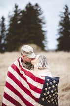 military couple wrapped in an American flag kissing 