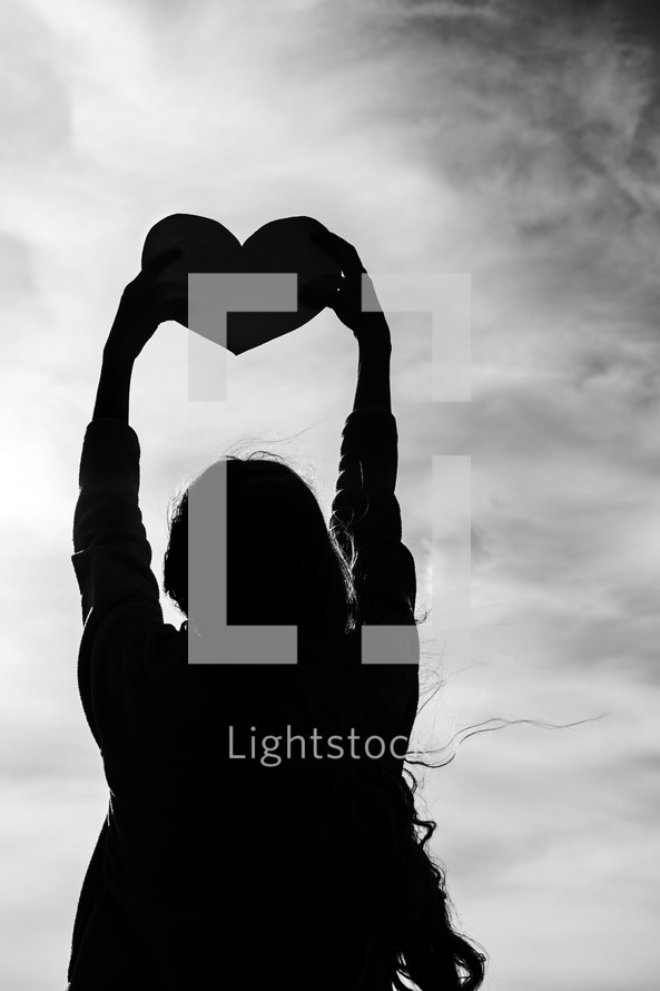 silhouette of a woman holding up a heart 
