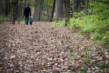 father and toddler son walking holding hands outdoors through fall leaves 