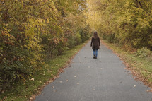 a woman walking on a paved path in fall 