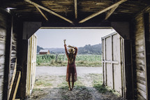 a woman in a dress and cowgirl hat standing at the entrance of a barn 