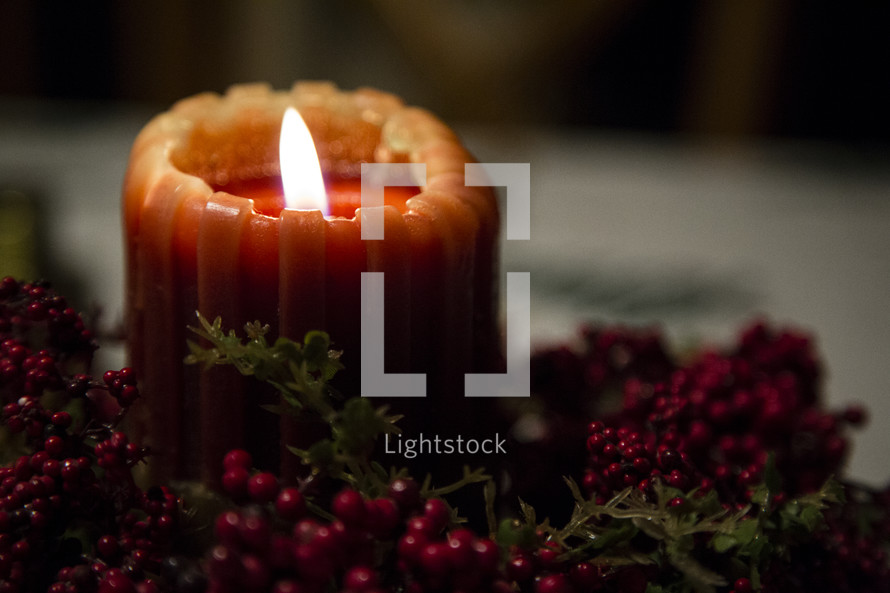 flame on a candle and berry garland 