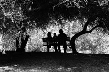 Man, woman and child sitting on a bench in a wooded area