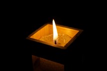 Lit votive candle in square wooden candle holder.