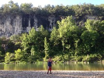 Child standing on the shore of a mountainside stream.