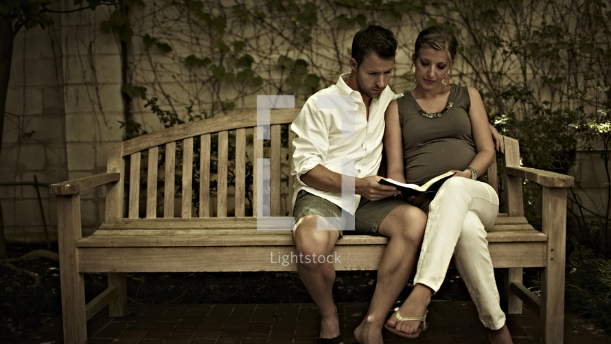 A man and woman reading the Bible on a bench.