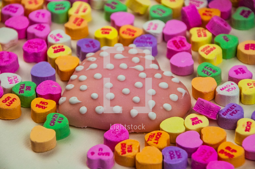 A heart shaped cookie surrounded by colorful Valentine candies.