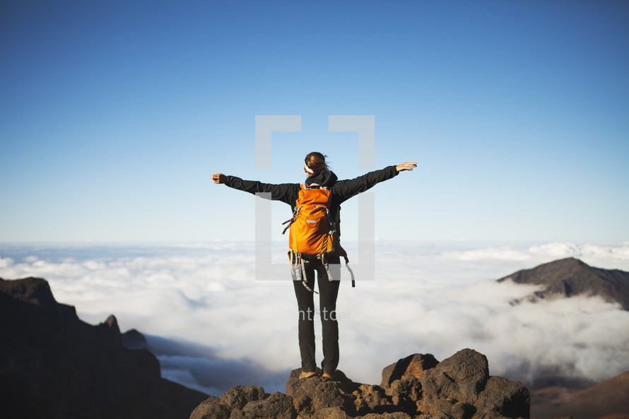 woman with outstretched arms standing at the top of a mountain 