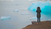 a woman in a coat looking out at icebergs 
