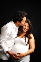 man kissing a pregnant woman on the forehead