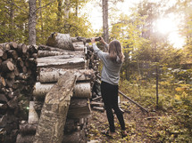 a woman getting firewood from a wood stack 