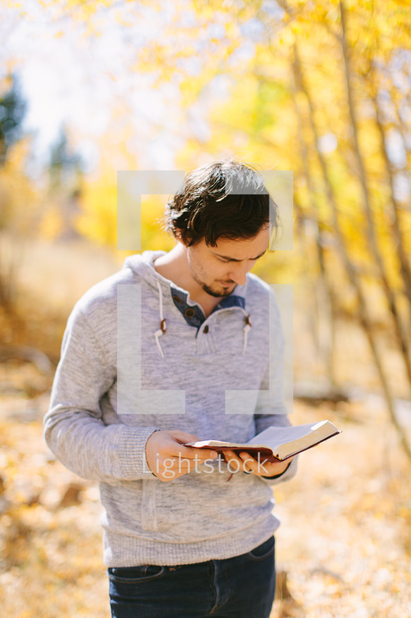 man standing outdoors reading a Bible on a fall day 