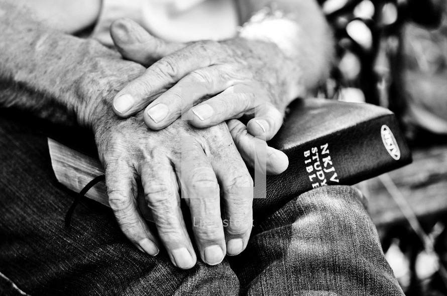 Elderly man's hands holding a Bible on his lap.