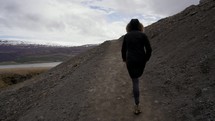 a woman in a coat walking on a dirt path 