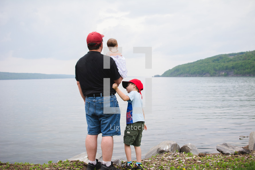 a father and his children standing on a lake shore 