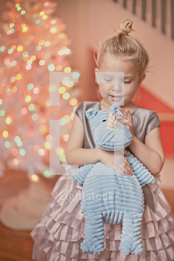 a little girl holding a stuffed animal in front of a Christmas tree