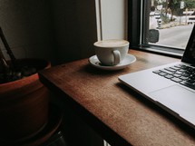 coffee cup and laptop computer on a wood desk in front of a window 