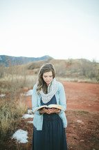 woman standing outdoors reading a Bible 