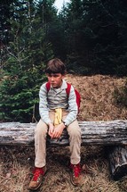 Eight year old boy sitting on a log to rest during a hike in the Adirondack mountains of upstate, New York. 