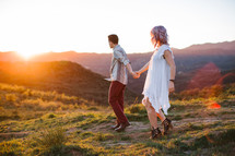 a couple walking holding hands on a mountaintop at sunset 