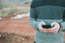man in a sweater texting outdoors