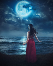 woman in a red dress looking at a full moon 