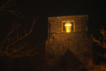 glowing cross in a church window at night 