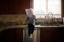 a girl sitting on a countertop in a kitchen reading papers 