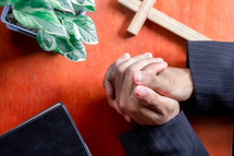 Close up hands praying on wooden table, view from above
