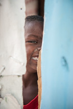 a smiling child peeking through a crack 