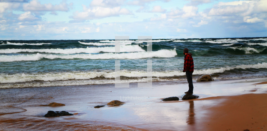 man standing on a rock on a beach 