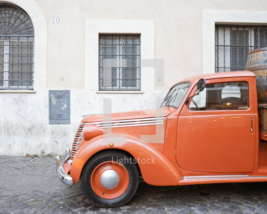 an old orange truck parked on a cobblestone street in Rome 