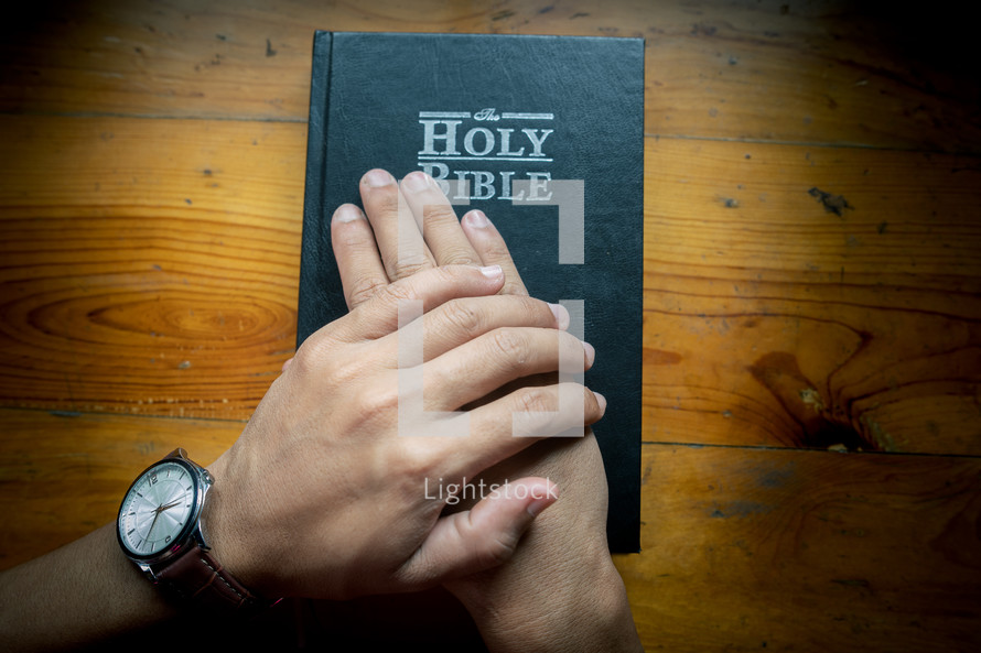 Hands pray on the holy Bible placed on a wooden table on Sunday. worship prayer and bible study concept.