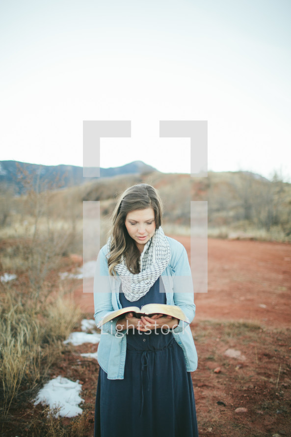 woman standing outdoors reading a Bible 