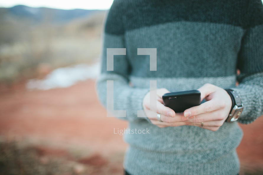 man in a sweater texting outdoors 