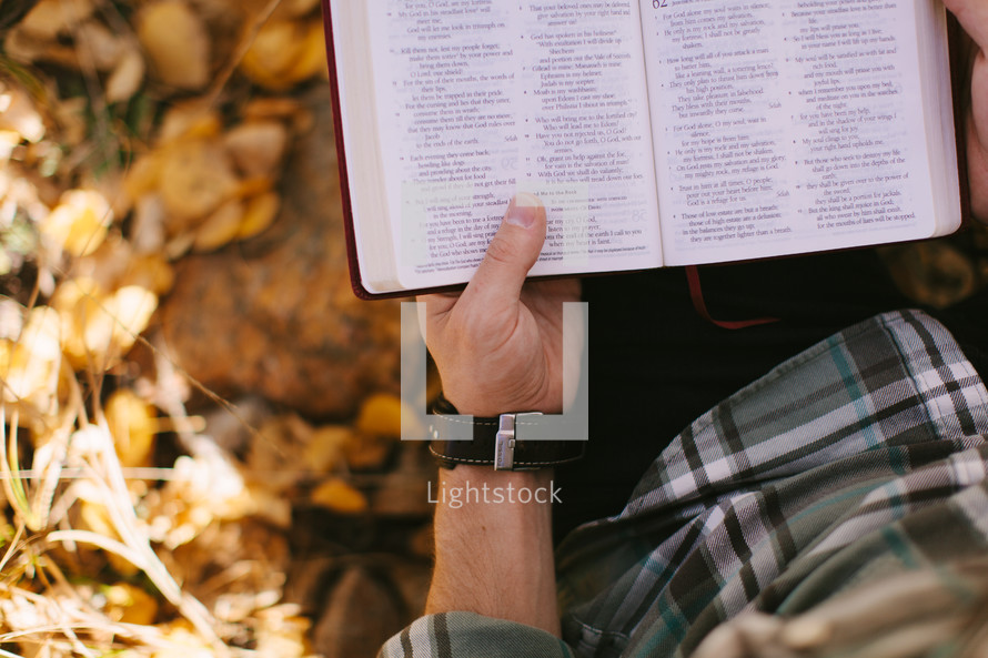a man sitting in fall leaves reading a Bible 