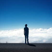 a teenage boy standing on a road above the clouds 