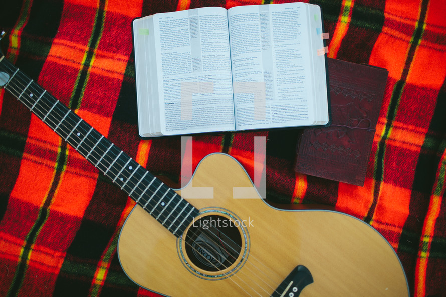 guitar, Bible, and journal on a plaid blanket 
