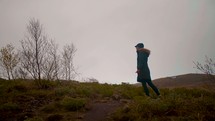 a woman walking up a grassy hill in a coat and gloves