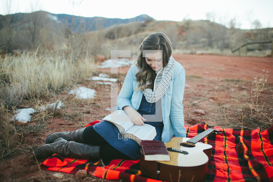 woman sitting on a plaid blanket with her guitar reading 