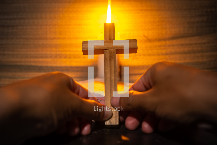 candle light with holy bible and hand holding cross on wooden table in the night time.