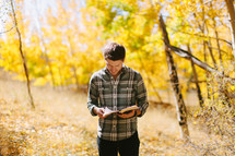 a man standing in a fall forest reading a Bible 