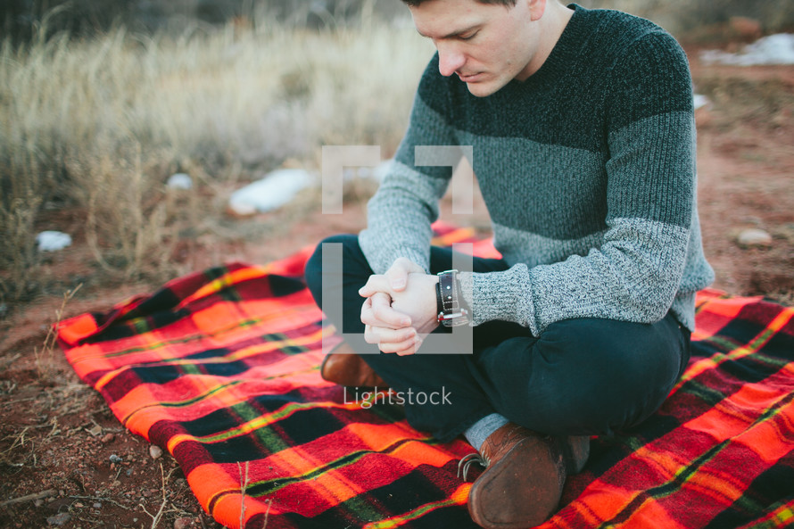 man on a plaid blanket with praying hands 