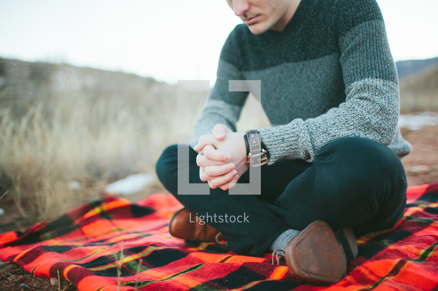 man sitting on a blanket praying 