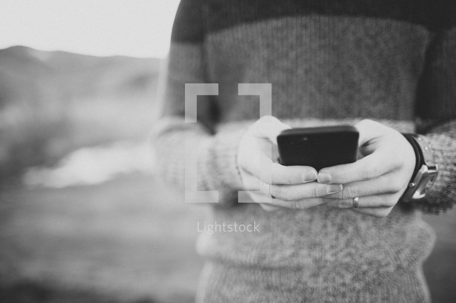 man in a sweater texting outdoors