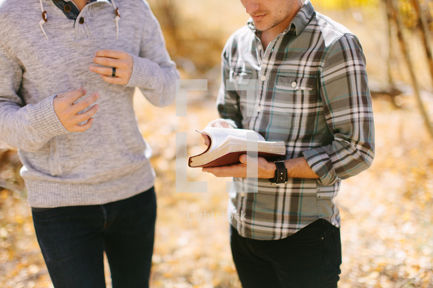 men standing together discussing a Bible on a fall day 