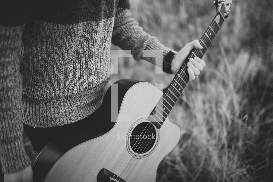 man in a sweater holding a guitar 