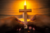 candle light with holy bible and hand holding cross on wooden table in the night time.